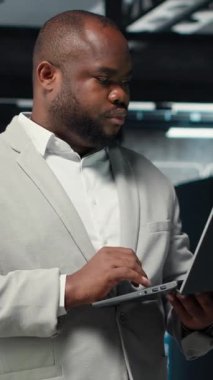 Veritabanında yürüyen dikey video teknisyeni, sistem istikrarını kontrol etmek için dizüstü bilgisayar kullanıyor. İşçi sunucu çiftliğini denetliyor, altyapıyı yapılandırmak için dizüstü bilgisayar kullanıyor, performansı optimize ediyor