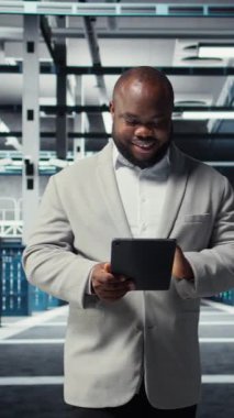 Dikey video mühendisi veri merkezinde yürüyor daha hızlı işlemek için tablet üzerindeki algoritmaları inceliyor. Altyapı kaynak optimizasyonu için sunucu çiftliği kodları yazan neşeli bir çalışan