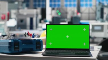 Yeşil ekranlı bir güneş enerjisi üretim tesisinde boş mühendislik masası. Robot kollar ve güneş paneli montaj hatlarıyla çevrili endüstriyel çalışma alanı. Performans izleniyor.