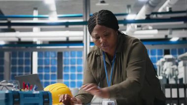 Afrikalı Amerikalı teknisyen üretim fabrikasında belgeler okuyor, kusursuz üretimi garanti altına almak için güneş panelleri ekipmanlarını inceliyor. Sürdürülebilir çözüm sistemi. Kamera A.