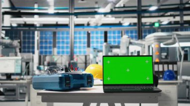 Güneş panellerindeki dizüstü bilgisayardaki izole kroma anahtar ekranı fabrika, sürdürülebilir çözümler ve temiz enerji için güneş pili mühendisliği. Yüksek teknolojili bir tesiste boş masa..