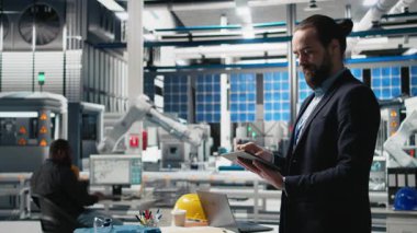 Endüstriyel erkek giysi uzmanı güneş enerjisi ekipmanlarını denetliyor, kalite kontrol ve üretim hattında verimlilik gösteriyor. Güneş panelleri üretiminde çalışıyorum. Kamera B.