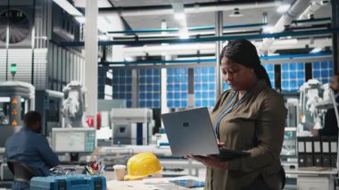 Fabrikadaki bilgisayar performans ölçümlerini kontrol eden siyah kadın mühendis, üretim tesisi, güneş panelleri üretimi ve endüstriyel işlemleri denetliyor. Yenilenebilir enerji. Kamera B.