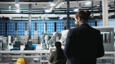 Güneş panelleri üretim hattını yöneten profesyonel mühendis, modern fabrikada ekipman ve verimliliği inceliyor. İş adamı uzmanı alternatif enerji üzerinde çalışıyor. Kamera B.