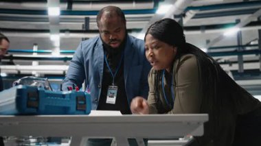 Afrikalı Amerikalı teknik uzmanlardan oluşan bir ekip, yenilenebilir enerji ve endüstriyel operasyonlarda gelecekteki gelişmeleri planlamak için yüksek teknoloji santralinde brifing üzerinde çalışıyor. Üretim süreci. Kamera B.