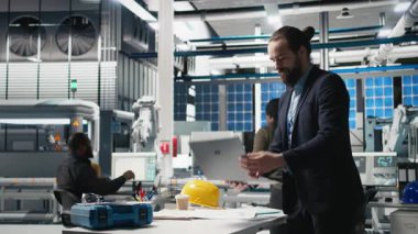 Takım elbiseli yönetici, bir güneş paneli fabrikasında modern imalatı ve alternatif enerji verimliliğini sembolize eden bir teftiş yapıyor. Üretim planlama ve teknoloji. Kamera B.