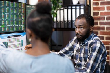 Siyahi erkek yöneticiye odaklanarak bilgisayar ekranındaki mali tabloları kadın çalışana açıkla. Afrika kökenli Amerikalı meslektaşlar modern ofisteki Forex ticaret verilerini analiz etmek için birlikte çalışıyorlar..