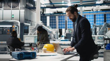 Güneş paneli montaj hattını izleyen bir giysi içindeki tesis denetleyicisi, profesyonel işgal ve yenilenebilir enerji büyümesine idari düzeyde katılımı yansıtıyor. Dayanıklılık. Kamera A.
