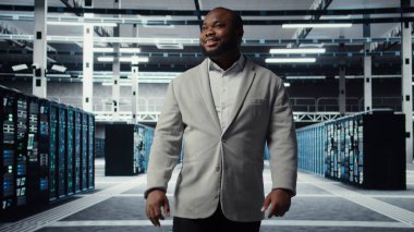 Gülümseyen bir çalışan yüksek teknoloji veri merkezinde ağları çalıştıran makinelerle yürüyor, şirketlerin veritabanlarını yönetiyor. Geniş veri işleme modülleriyle sunucu çiftliğini denetleyen yönetici, kamera A