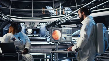 Astronot, uzay istasyonu dışında planlanan operasyonlara girmeden önce gezegen görselleştirmesine bakıyor. Uzay gemisindeki kozmonot gelişmiş mühendislerin gezegene inmesiyle çalışıyor.