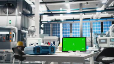 Robotik kolların fotovoltaik panel montaj sürecini düzene soktuğu bir güneş enerjisi tesisinde güvenlik gözlükleri ve bilgisayar ekranlı boş masa ve çalışma alanı. Performans ölçümleri.