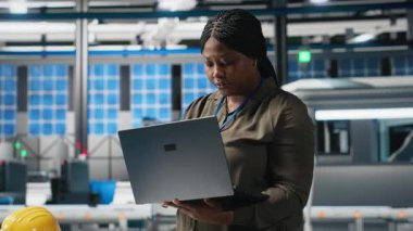 Fabrikadaki bilgisayar performans ölçümlerini kontrol eden siyah kadın mühendis, üretim tesisi, güneş panelleri üretimi ve endüstriyel işlemleri denetliyor. Yenilenebilir enerji. Kamera A.