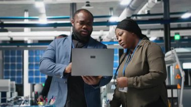 Afrika kökenli Amerikalı endüstriyel çalışanlar güneş panelleri için üretim hattı üzerinde takım çalışması yapıyorlar, teknik içgörü ve takım çalışmasını birleştirerek temiz enerji altyapısını ileriye taşıyorlar. Kamera A.