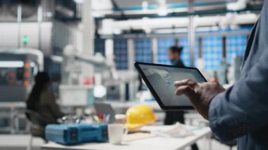 Sanayi uzmanı tabletteki dijital üretim sistemlerini fabrikadaki güneş enerjisi üretim hattını kontrol ediyor. Siyahi uzmanlar güneş santralinde endüstri mühendisliği gösteriyor. Kapatın. Kamera B.