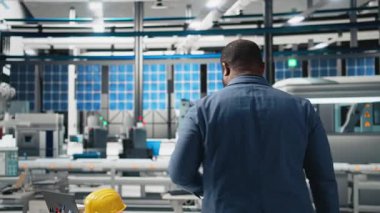 Afro-Amerikan endüstrisi uzmanı fotovoltaik üretim hattını inceliyor, güneş enerjisi sektöründe verimliliği sağlamak için üretimi inceliyor. Genç mühendis bir fabrikada. Kamera B.