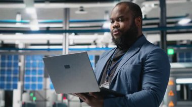 Bir güneş paneli tesisinde Afrika kökenli Amerikalı yönetici performans ve verimlilik ölçümlerini izliyor, gerçek zamanlı kalite kontrolü ve stratejik iş geliştirme ile liderliği birleştiriyor. Kamera A.