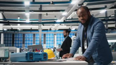 Afrika kökenli Amerikalı endüstriyel uzmanlar, güneş panellerini kağıtlardaki modellerle inceliyor, sürdürülebilirliği, yenilenebilir enerjiyi ve modern fabrikayı garanti altına almak için önemli içgörüler okuyor. Kamera B.