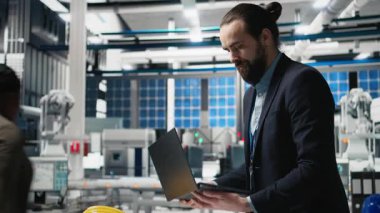 Güneş paneli montaj hattını izleyen bir giysi içindeki tesis denetleyicisi, profesyonel işgal ve yenilenebilir enerji büyümesine idari düzeyde katılımı yansıtıyor. Dayanıklılık. Kamera B.