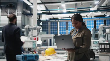 Afrika kökenli Amerikalı kadın, endüstriyel işlemleri gösteren alternatif enerji üretiminde kullanılan güneş panelleri fabrikasında sistem kontrollerini kontrol ediyor. Mühendislik. Kamera B.