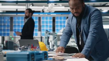 Siyah usta mühendis, imalat fabrikasında alternatif enerji sistemleri üzerinde çalışan fotovoltaik üretim hattı ekipmanlarını inceliyor. Güneş enerjisi endüstrisinde uzman. Kamera A.