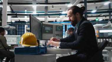 Güneş panelleri santralindeki bilgisayar görüşünü inceleyen profesyonel mühendis, üretim hattı ve kalkınma hedefleri için alternatif enerji sistemlerini güvence altına almak için bir teftiş yapıyor. Kamera B.