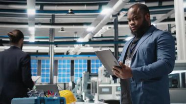 Siyah endüstri uzmanı yenilenebilir enerji başarısını sürdürmek için yenilik ve verimlilik sağlayan bir güneş teknolojisi tesisinde üretim verilerini inceliyor. Çevre dostu sürdürülebilir çözümler. Kamera B.