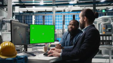 Usta mühendislerden oluşan çeşitli ekipler, güneş enerjisi santralinde üretimde kullanılan izole bir ekran ile çalışmakta, teknik gelişim için fikirleri ve stratejik planlamayı paylaşmaktadır. Kamera B.