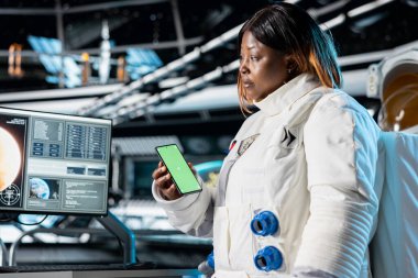 İzole edilmiş cep telefonu tutan kadın astronot bilim adamı monitöre bakıyor. Uzay gemisinde kozmonot kıyafeti giyen kadın araştırmacı model akıllı telefon kullanıyor, araştırma yapıyor.