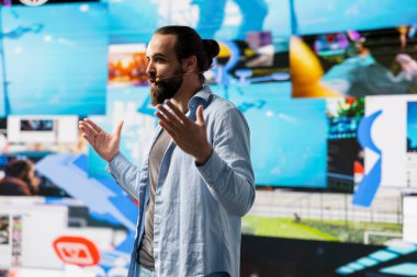 Erkek canlı sunucu çevrimiçi bir izleyiciye markalaşma stratejisi ve sosyal eğilimler hakkında iletişim kuruyor, sunum sırasında mikrofon kullanarak katılım ve küresel erişimi artırıyor.