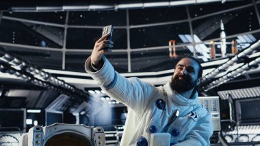 Astronot akıllı telefonuyla özçekim fotoğrafları çekiyor. Gezegen kolonileştirme görevi sırasında el hareketi yapıyor. Yörünge istasyonu mürettebatı kozmik yolculuk sırasında cep telefonuyla fotoğraf çekiyor.