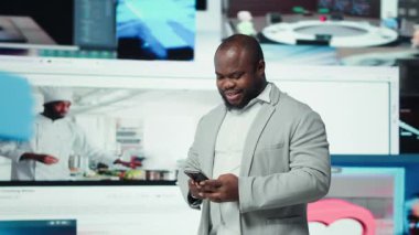 Sosyal ağlarda gezinen gülümseyen bir adamın portresi video baykuşunun önünde akıllı telefondan besleniyor. Neşeli Afrikalı Amerikalı telefon kullanıyor, interaktif bağlılığı vurgulayan yüzen simgeler, kamera A