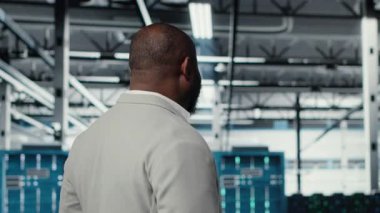 Veri merkezinde yürüyen mutlu işadamı yatırım yapmadan önce paraşütlerin kapasitesini ölçüyor. Jolly yönetim yöneticisi sunucu çiftliği işletme depolama teçhizatı için inşa edildi, kamera B