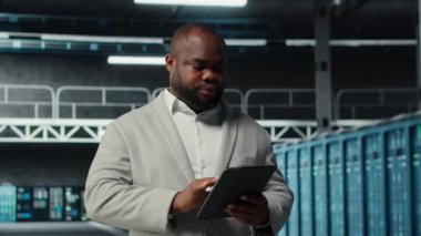 System administrator walking in server farm deploying infrastructure for efficient data analysis. Worker using device in dat a center in managing storage systems for datasets, camera B