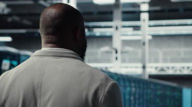 Veri merkezindeki sistem yöneticisi altyapı teknisyenlerinin kullanıcı taleplerini denetliyor. Sunucu çiftliğindeki Afrikalı Amerikalı işçiler ekipmanların trafik modellerini analiz ediyor, kamera B