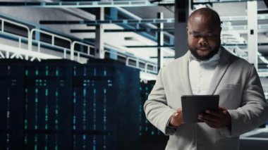 Veri merkezinde yürüyen teknisyenlerin sistem istikrarını kontrol etmek için tablet kullanmalarını kapatın. IT uzmanı sunucu çiftliğini denetliyor, donanımları ayarlamak için aygıt kullanıyor, performansı optimize ediyor, kamera A