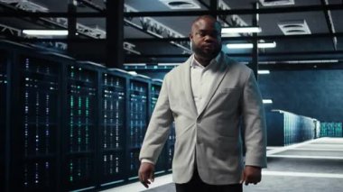 Server farm admin overseeing supercomputers, troubleshooting bugs. African american manager walking in data center, doing inspection to ensure error free equipment, camera A