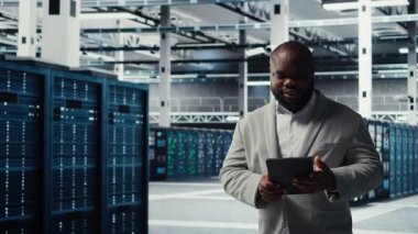 Sistem istikrarı için yazılım güncellemelerini yönetmek için tablet kullanan neşeli veri merkezi programcısı. Neşeli sunucu odası bilişim uzmanı cihaz ile performansı optimize ediyor, altyapı yapısını yapılandırıyor, kamera A