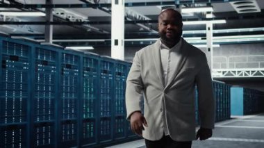 Sunucu merkezindeki gülümseyen mühendis veri merkezinin enerji tüketimini bileşenler arasında izliyor. Veri merkezinde yürüyen mutlu bilişim uzmanı, sondaj sensörlerinin en uygun şekilde çalıştığından emin oluyor.