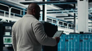 Sistem istikrarı için yazılım güncellemelerini yönetmek için dizüstü bilgisayar kullanan veri merkezi teknisyeni. Afro-Amerikan sunucu odası IT profesyoneli performansı optimize ediyor, altyapıyı yapılandırıyor, kamera B