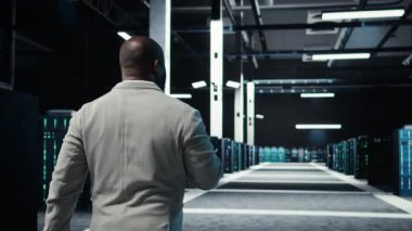 Sunucu odası yazılım geliştiricisi dizüstü bilgisayardaki yazılımı kullanarak hata yaptı. Afrika kökenli Amerikalı bilişim uzmanı veri merkezinde yürüyor. Not defteri, kamera A kullanarak hata düzeltme yapıyor.