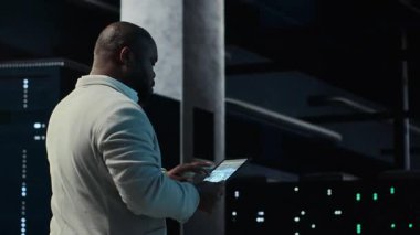 Software developer in data center using tablet, employing AI machine learning models. Employee using device to fulfill artificial intelligence infrastructure needs, allocating resources, camera B