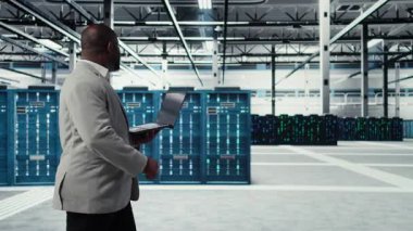 Sistem istikrarını yükseltmek için dizüstü bilgisayar kullanan gülümseyen bir veri merkezi programcısı. Neşeli Afro-Amerikan sunucu merkezi bilişim uzmanı kodlama, cihaz ile performansı optimize etme, ayarlama ekipmanları, kamera A