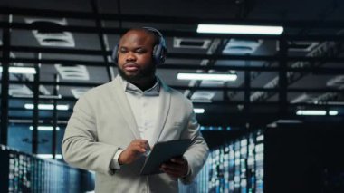 Veri Merkezi yöneticisi, kulaklık takıyor. Dar boğazları tanımlamak için tablet kullanıyor. Sunucu çiftliği bilişim uzmanı, sorun yaratan hataları dinlerken müzik dinliyor, iyileştirmeler yapılıyor, kamera B