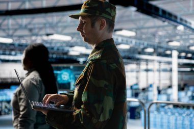 Soldier maintaining secure military networks inside data center facility. Army information technology professional in server room monitoring classified systems using laptop