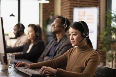 Masaüstü bilgisayarında müşteri geri bildirimini inceleyen Asyalı bir çalışan servis kalitesini artırmak için strateji geliştiriyor. Bir kulaklık takan, bir başlangıç ofisinde klavyeye yazan kadın istemci destek aracıName.