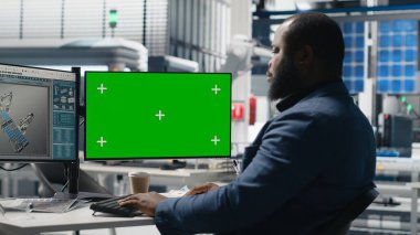 PC 'nin yanındaki montaj hattını inceleyen erkek teknoloji uzmanı, yeşil enerjinin etkin kalite kontrolü ve taahhütünü sağlamak için güneş enerjisi santralindeki fabrika operasyonlarını yönetiyor. Kamera B.