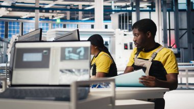 Siyah çalışan, güneş paneli konfigürasyonunu masaüstü araçları, fabrika üretimini optimize etme ve sorun giderme yoluyla yönetiyor. Teknisyen enerji sistemi parametrelerini bilgisayarda güncelliyor. Kamera B.