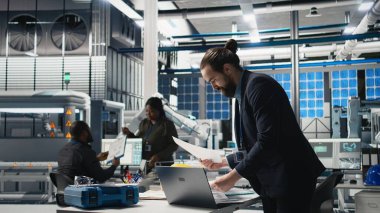 Takım elbiseli yönetici, bir güneş paneli fabrikasında modern imalatı ve alternatif enerji verimliliğini sembolize eden bir teftiş yapıyor. Üretim planlama ve teknoloji. Kamera A.