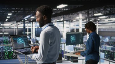 Veri merkezindeki programcı ve meslektaşım bilgisayardaki AI LLM görselleştirmelerini inceliyor. IT ekip çalışanları, istikrarlı altyapı işlemleri sağlamak için nöral ağ performans çıktılarını analiz ederler