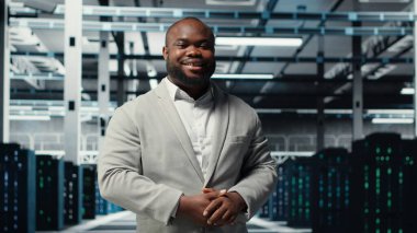 Veri merkezindeki gülümseyen müdür devre dışı kalmamak için donanım kontrolü yapıyor. Mutlu Afro-Amerikan Denetleyici sunucu odası altyapı süper bilgisayarları, kamera B